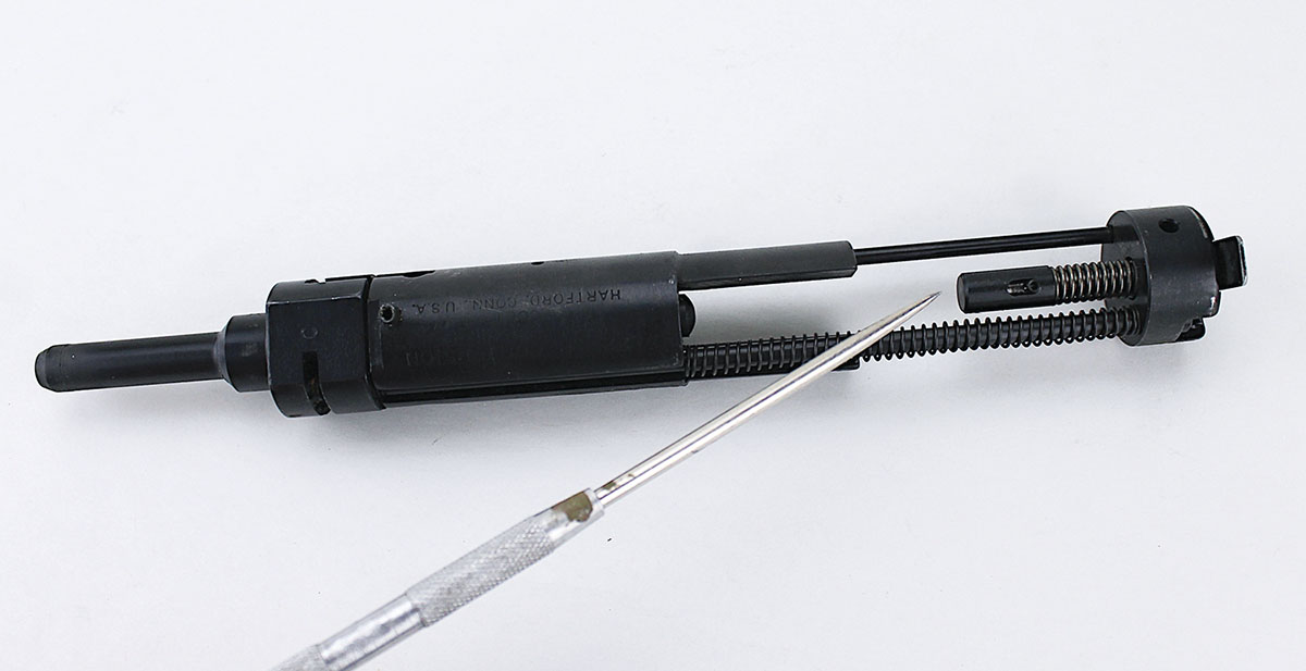 As the bolt recoils backward, the back of the firing pin contacts this post, spring and plunger assembly, making the firing pin serve double duty as  the ejector.